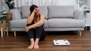 Woman sits on floor next to scale