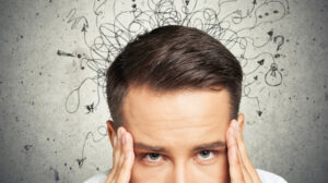 man holding his temples with scribble on the wall behind