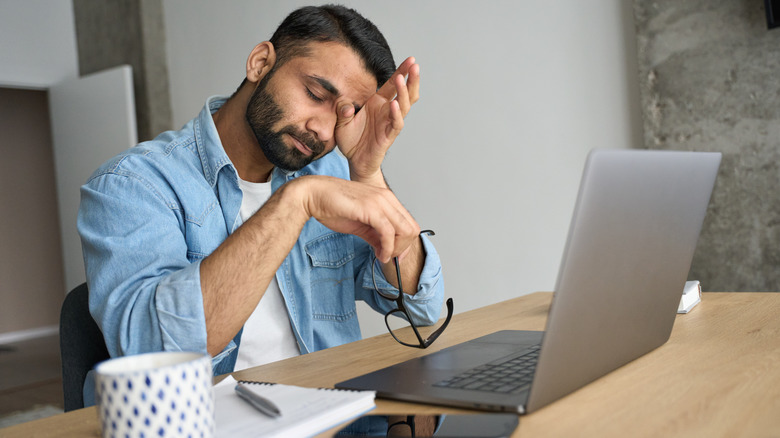 stressed out man wiping his tired eyes at his laptop