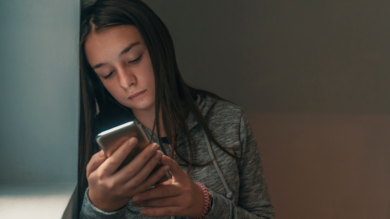 Sad young girl looking at smartphone