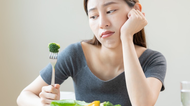 Asian girl looking unhappily at broccoli
