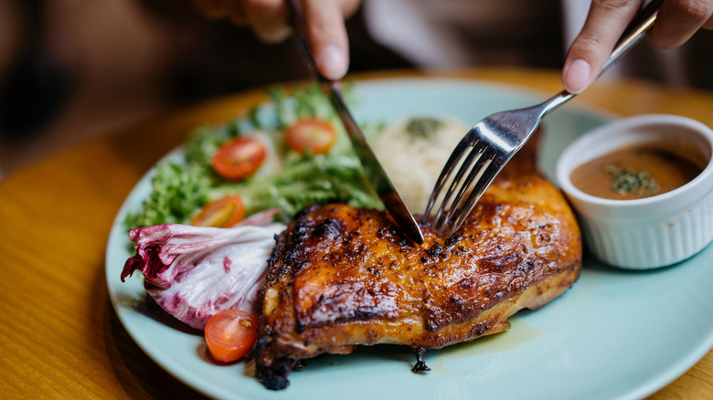 Hands using utensils to cut chicken meat