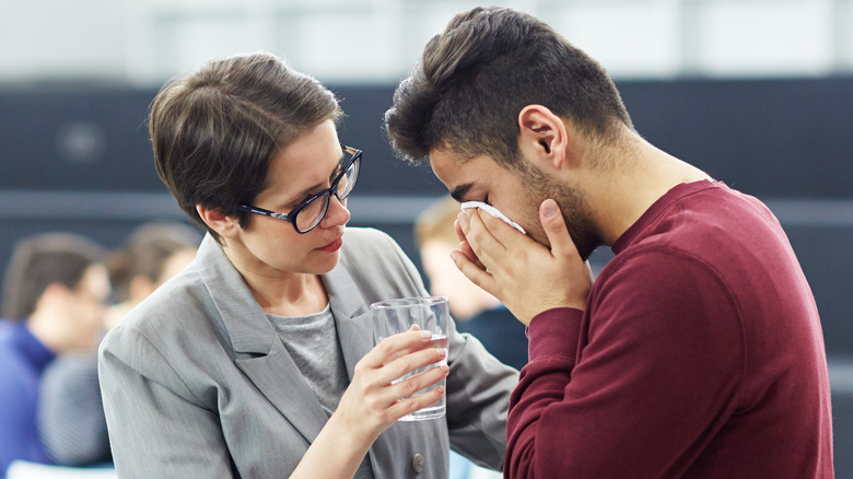 Coworker handing crying man water glass