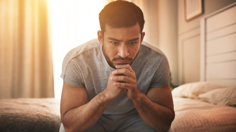 man sitting on the edge of his bed feeling depressed