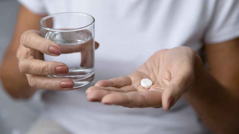 Hand holding pill and glass of water
