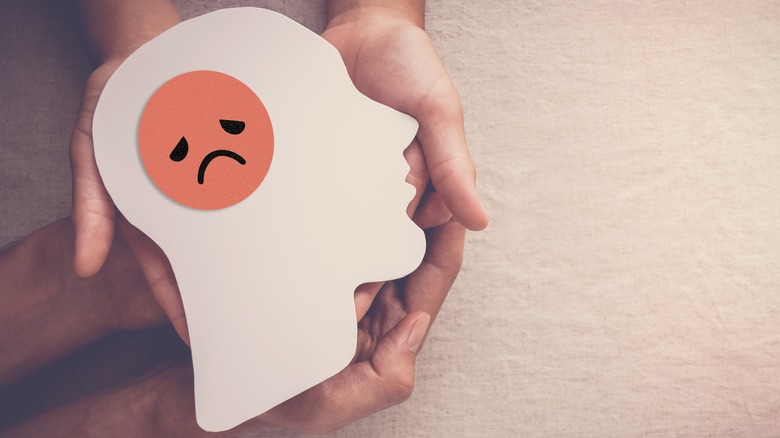 Hands holding the image of a human head with a frowning brain